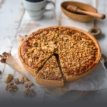 Tarta de Cerrobayo artesanal cubierta con una generosa capa de nueces y frutos secos, con una porción cortada, junto a una taza de café en Panadería El Molino, Cali.