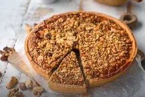 Tarta de Cerrobayo artesanal cubierta con una generosa capa de nueces y frutos secos, con una porción cortada, junto a una taza de café en Panadería El Molino, Cali.