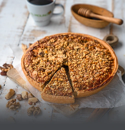 Tarta de Cerrobayo artesanal cubierta con una generosa capa de nueces y frutos secos, con una porción cortada, junto a una taza de café en Panadería El Molino, Cali.