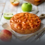 Tarta vienesa de manzana entera y artesanal con cubierta dorada y brillante, servida sobre una tabla rústica junto a manzanas frescas en Panadería El Molino, Cali.