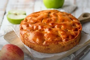 Tarta vienesa de manzana entera y artesanal con cubierta dorada y brillante, servida sobre una tabla rústica junto a manzanas frescas en Panadería El Molino, Cali.