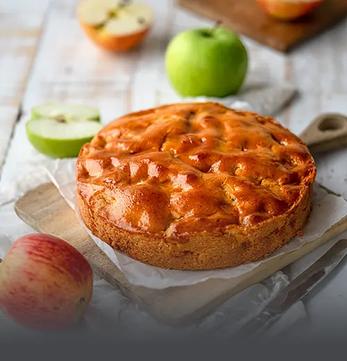 Tarta Vienesa de Manzana Entera - Panadería El Molino Cali Tarta vienesa de manzana entera y artesanal con cubierta dorada y brillante, servida sobre una tabla rústica junto a manzanas frescas en Panadería El Molino, Cali.