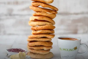 Pila de tostadas saladas artesanales y muy crujientes, acompañadas de mantequilla, mermelada y una taza de café con el logo de Panadería El Molino, Cali.