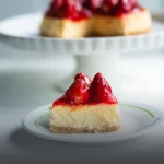 Porción de cheesecake artesanal con cobertura de fresas brillantes, servida en un plato con el logo de Panadería El Molino, con el cheesecake entero al fondo desenfocado.