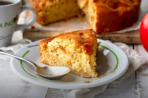 Porción individual de tarta vienesa de manzana artesanal servida en un plato con el logo de Panadería El Molino, acompañada de la tarta entera y café en Cali.