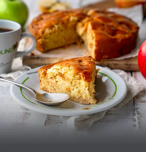 Porción Tarta Vienesa de Manzana - Panadería El Molino Cali Porción individual de tarta vienesa de manzana artesanal servida en un plato con el logo de Panadería El Molino, acompañada de la tarta entera y café en Cali.
