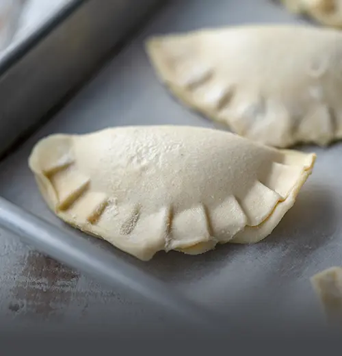 Bandeja de Empanadas de Ricota y Espinaca para Hornear - Panadería El Molino Cali Bandeja con empanadas artesanales crudas rellenas de ricota y espinaca, listas para hornear en casa, elaboradas por Panadería El Molino en Cali.