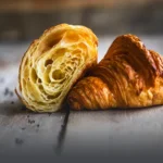 Croissant parisino artesanal con capas de hojaldre definidas, dorado y brillante sobre una mesa de madera rústica en Panadería El Molino, Cali.