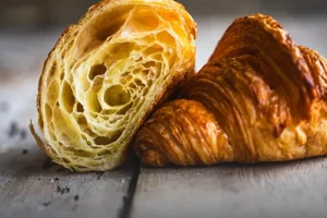 Croissant parisino artesanal con capas de hojaldre definidas, dorado y brillante sobre una mesa de madera rústica en Panadería El Molino, Cali.