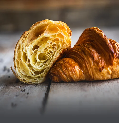 Croissant parisino artesanal con capas de hojaldre definidas, dorado y brillante sobre una mesa de madera rústica en Panadería El Molino, Cali.