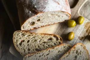 Hogaza de pan de masa madre con olivas verdes, cortada en rebanadas sobre una tabla de madera rústica, resaltando la miga con trozos de aceituna en Panadería El Molino.