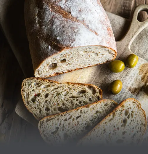 Hogaza de pan de masa madre con olivas verdes, cortada en rebanadas sobre una tabla de madera rústica, resaltando la miga con trozos de aceituna en Panadería El Molino.