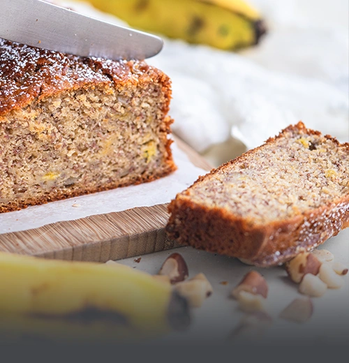 Porción de cake artesanal de banano y nuez siendo cortada, servido junto a bananos frescos y trozos de nuez en Panadería El Molino, Cali.