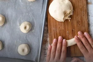Manos moldeando masa cruda de pandeyuca sobre una tabla rústica, junto a una bandeja lista para hornear en casa, de Panadería El Molino, Cali.