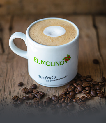 Taza de café caliente y espumoso con el logo de Panadería El Molino, rodeada de granos de café tostado. La bebida perfecta para acompañar tu pan artesanal en Cali.