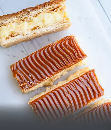 Deliciosas milhojas artesanales de hojaldre crujiente, rellenas de crema y cubiertas con abundante arequipe. Postre tradicional y fresco de Panadería El Molino en Cali.