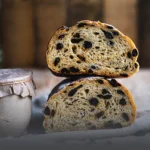 Dos mitades de pan artesanal de avena y pasas mostrando una miga suave y llena de uvas pasas, junto a un frasco rústico en Cali.
