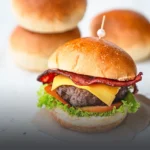 Pan de papa suave y dorado para súper hamburguesa gourmet, presentado junto a una hamburguesa con carne, queso y tocineta en Cali.