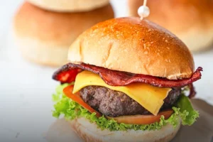 Pan de papa suave y dorado para súper hamburguesa gourmet, presentado junto a una hamburguesa con carne, queso y tocineta en Cali.