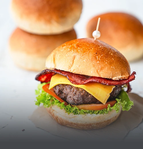 Pan de papa suave y dorado para súper hamburguesa gourmet, presentado junto a una hamburguesa con carne, queso y tocineta en Cali.