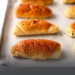 Panes suaves de mantequilla dorados y recién horneados sobre una bandeja de panadería en Cali.