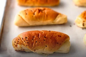 Panes suaves de mantequilla dorados y recién horneados sobre una bandeja de panadería en Cali.
