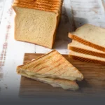 Bloque y rebanadas de pan de molde grande artesanal junto a un sándwich tostado con queso derretido en Cali.