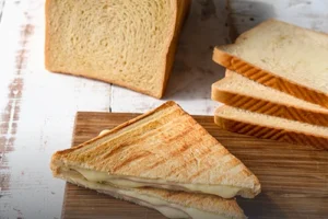 Bloque y rebanadas de pan de molde grande artesanal junto a un sándwich tostado con queso derretido en Cali.