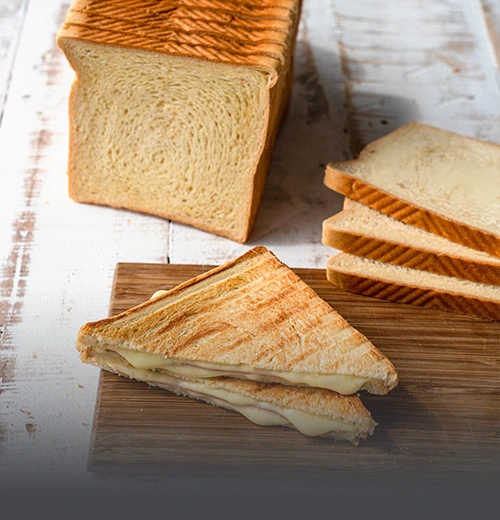 Bloque y rebanadas de pan de molde grande artesanal junto a un sándwich tostado con queso derretido en Cali.