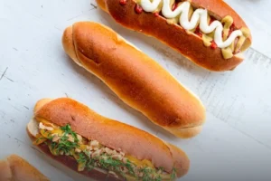 Panes artesanales para perro caliente recién horneados sobre una mesa blanca, algunos decorados con salsas y aderezos en Cali.